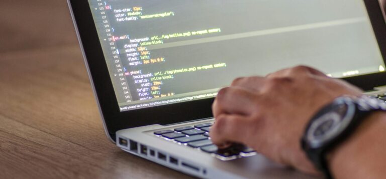 A close-up shot of a person coding on a laptop, focusing on the hands and screen.